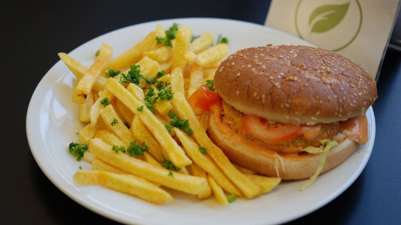 Veganer Burger mit Kürbis-Chiasamen-Patty (A, A1, J, K) mit Tomate, Röstzwiebeln, Salat, Burgersoße und Gurke, dazu Pommes frites